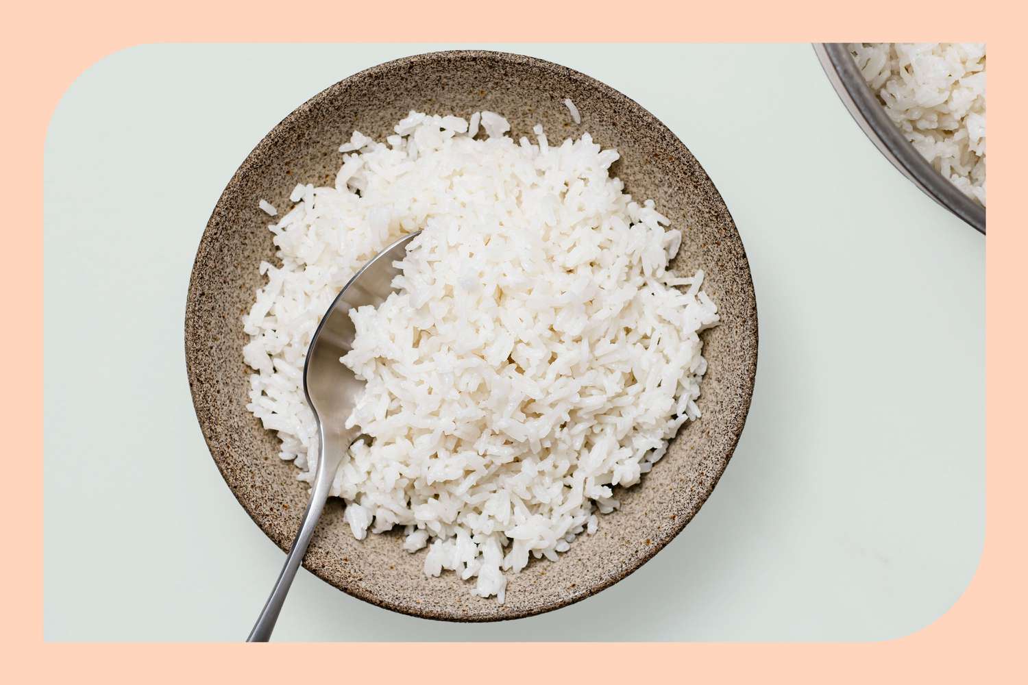 An earthenware bowl filled with white rice with a serving spoon sticking out