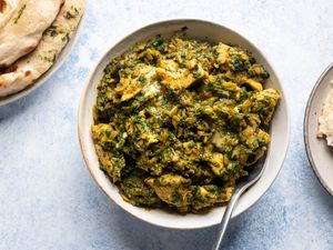 overhead shot of Chicken Saagwala in a white bowl surrounded by plates of naan