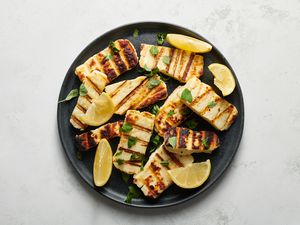 grilled halloumi cheese served on a plate with lemon wedges and herbs