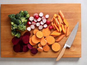 broccoli, radishes, carrots, beets, and yams cut on cutting board with a knife