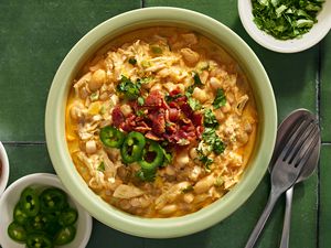 A bowl of jalapeÃ±o popper chili topped with chopped cilantro, sliced jalapeÃ±os, and crumbled bacon