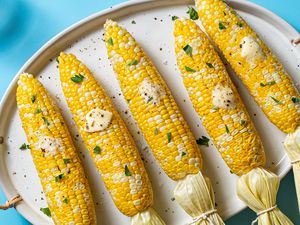 microwaved corn on the cobs on a serving platter with butter, parsley, and salt and pepper