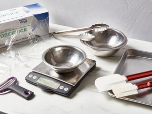 Plastic wrap, Y peeler, digital kitchen scale, metal mixing bowls, metal tongs, rubber spatulas, and a sheet tray