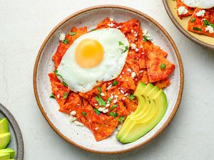 A serving of chilaquiles, stopped with a fried egg and served with sliced avocado