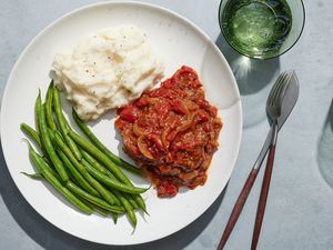 A plate of Swiss steak served with steamed green beans, mashed potatoes, and sparkling water