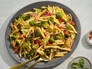 A large bowl of pasta primavera served with basil leaves and red pepper flakes