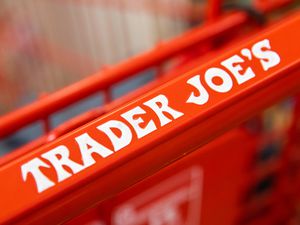 A close up of a Trader Joe's shopping cart handle that says "Trader Joe's" on it