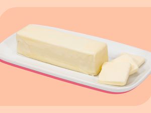 A stick of butter sitting on the bottom part of a ceramic butter dish