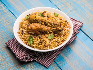 Indian biryani in a white bowl on top of a checkered napkin on a blue wooden surface