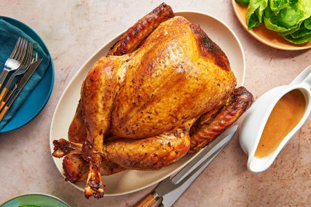 A garlic and scallion-soy sauce whole turkey served on a platter, with gravy and green salad on the side.