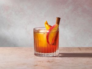 An apple cider old fashioned cocktail, garnished with a slice of apple, an orange peel, and a cinnamon stick