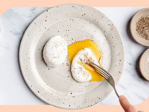 Two poached eggs on a speckled stoneware plate showing a fork cutting into one of the eggs and the runny yolk oozing out