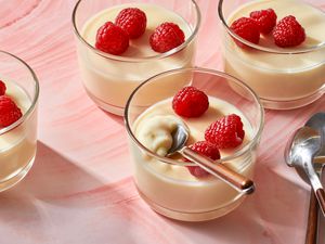 Four glasses of lemon posset topped with fresh raspberries