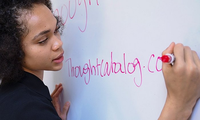 Frau erklärt etwas, während sie mit einem roten Stift auf ein Whiteboard schreibt