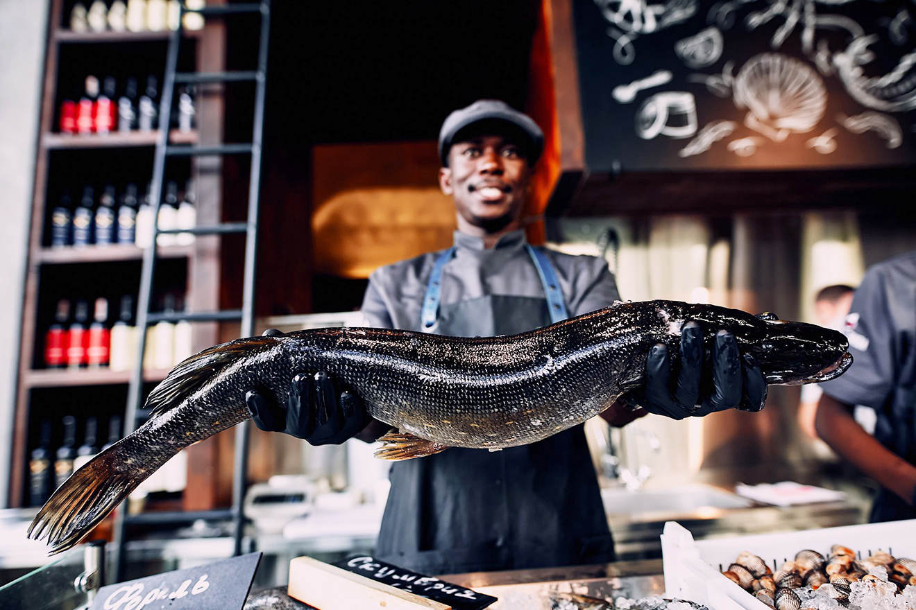 A smiling chef proudly holds up to the camera a medium size fish, ready for culinary creations.