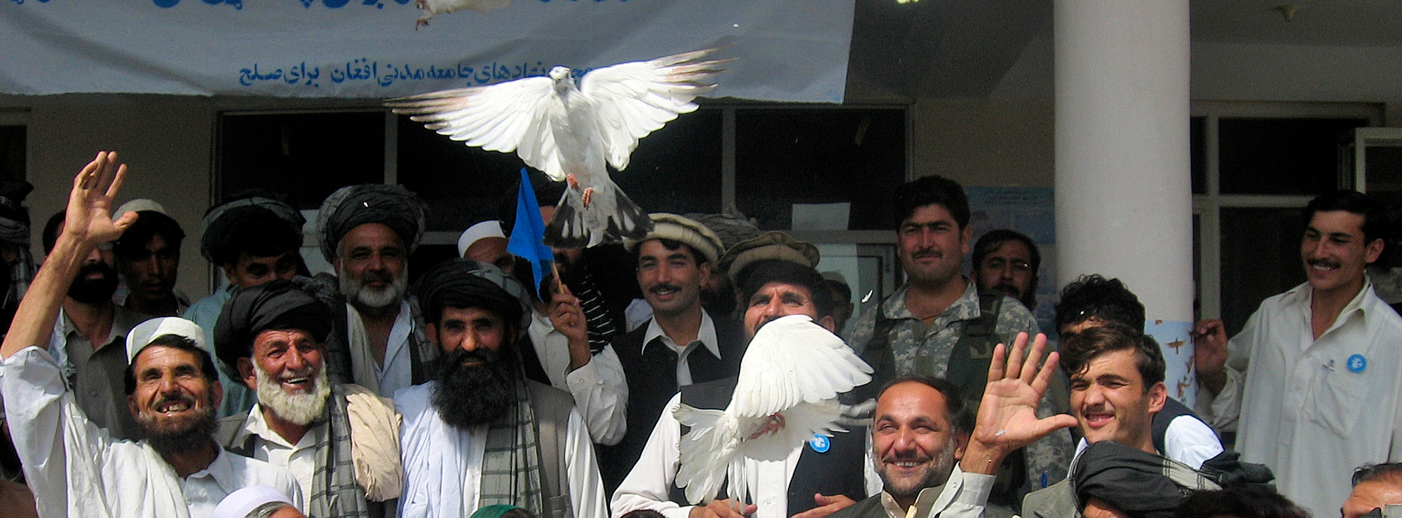 A crowd smiles and looks up as white doves fly away.