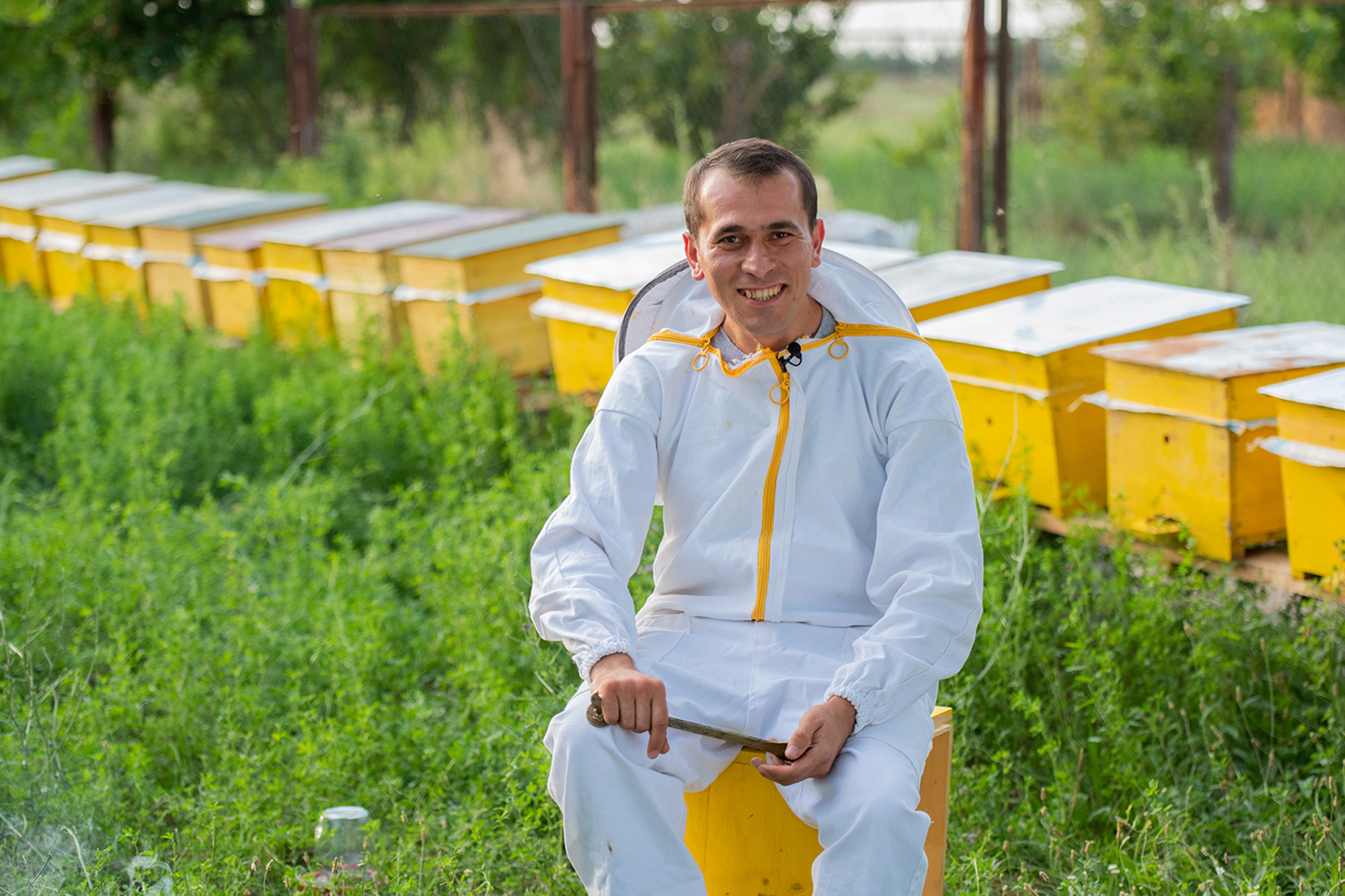 An Azerbaijani beekeeper stands in front of a row of beehives.