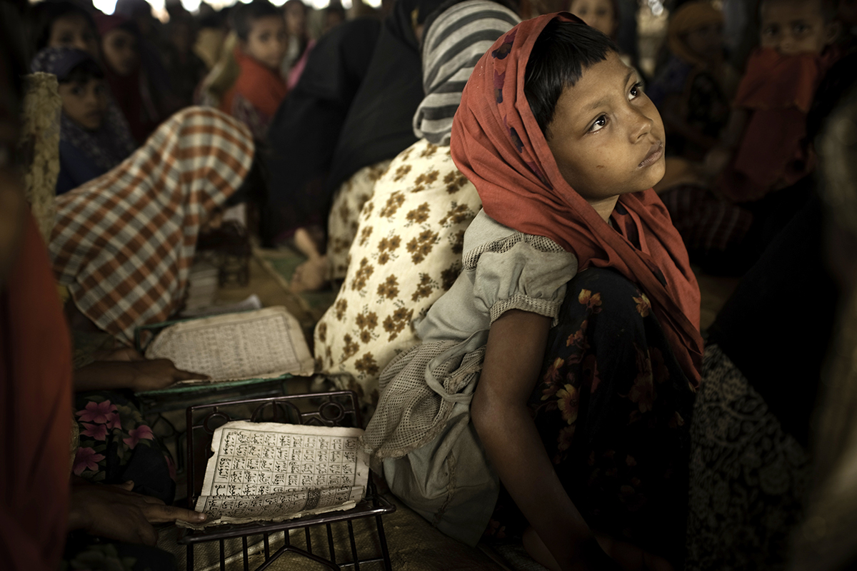 A girl sits on the ground among a large group of children in a class. 