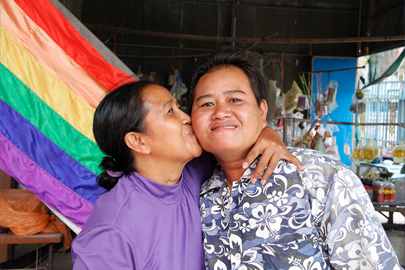 Sao Mimol kisses her partner with a flag of LGBT pride behind them