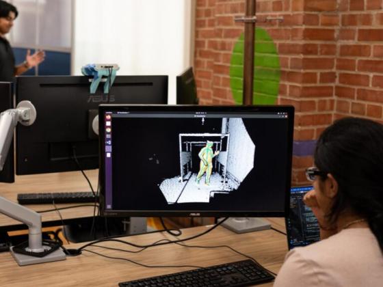 woman working at computer with person's outline on screen and person in background