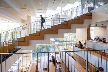 A student walks down a staircase while other students study in the atrium below