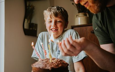 A child sitting behind a birthday cake as a man lights the candles