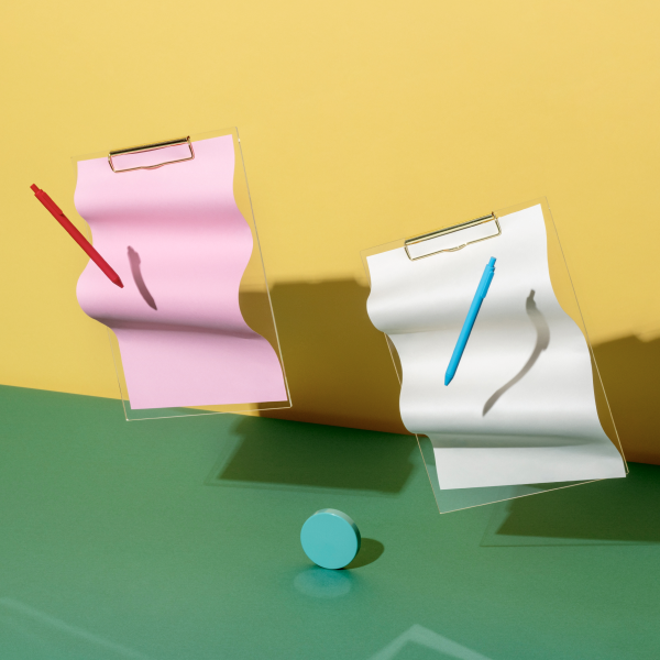 Stylized clipboards and pens suspended over a colorful desk and backdrop.