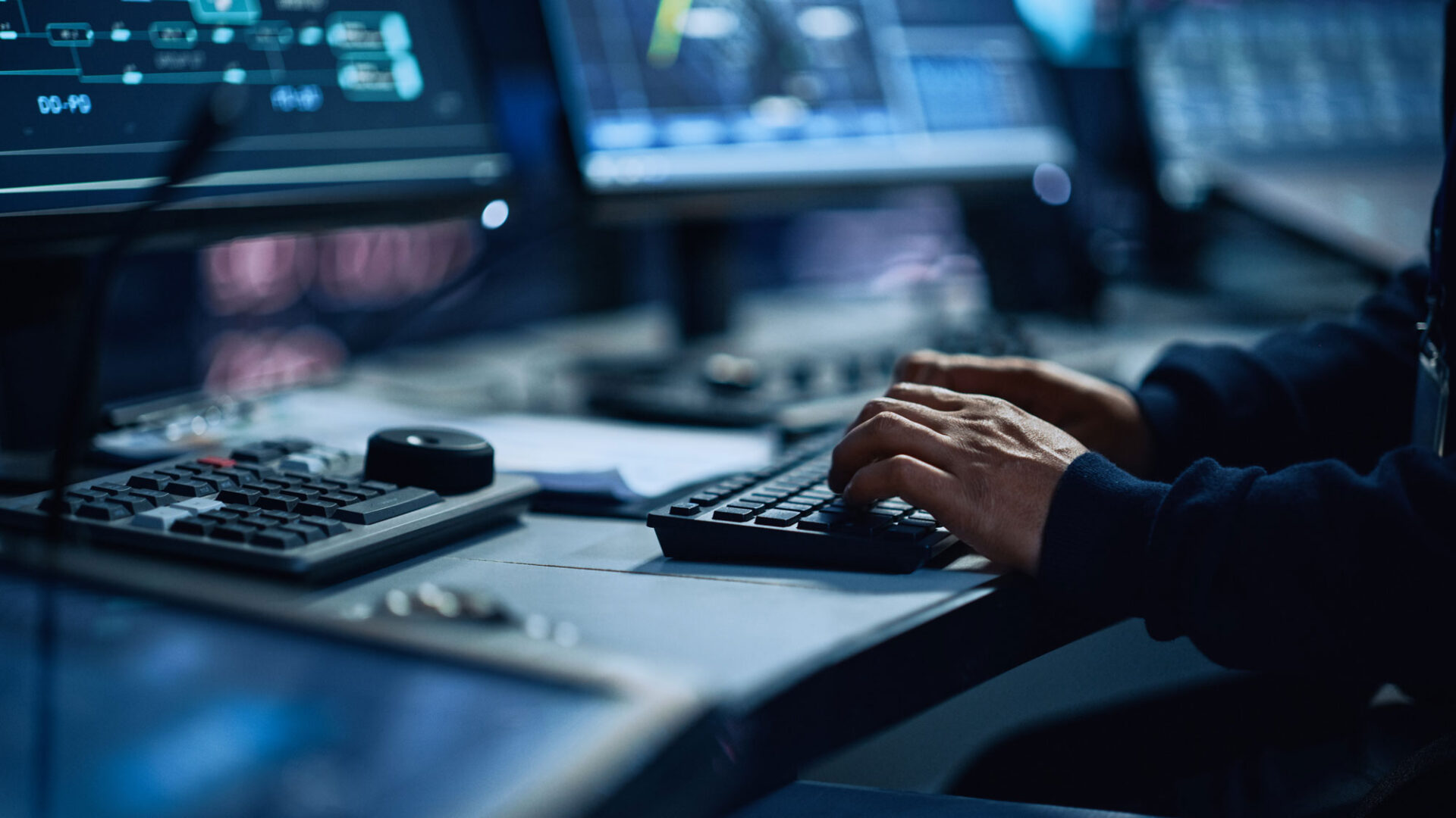 a close up photo of someone typing on a keyboard connected to multiple data-centered monitors