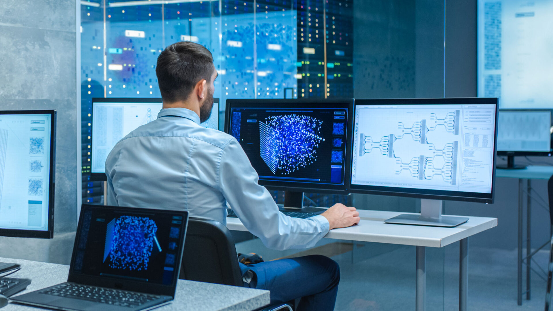 a man working in a high tech office on a series of monitors looking at analytics