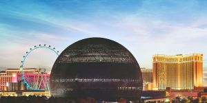 A large black sphere dominates the Las Vegas skyline. A Ferris wheel is on the left in the background, and other buildings can be seen as well. The sky is blue, but the foreground is dark.