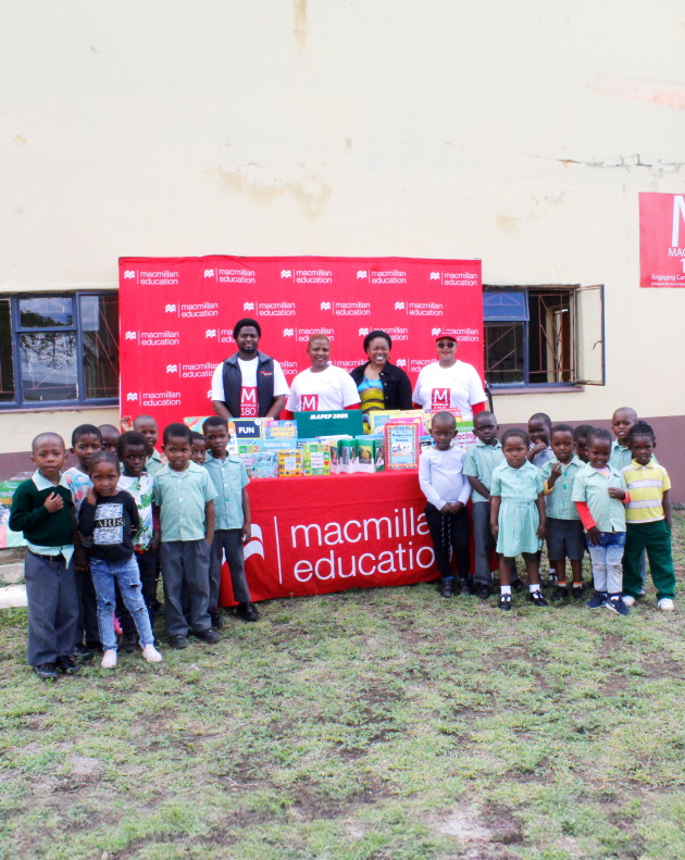 A macmillan education stall. There are four people standing behind the stall. Many children are standing in front at the sides of the stall.