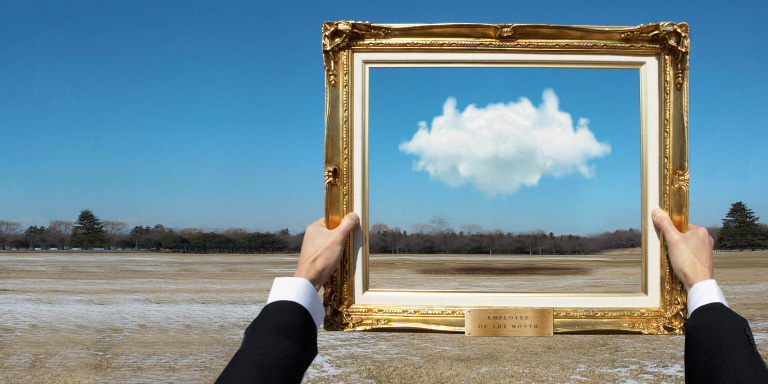 A pair of hands holding a golden decorative frame to highlight a single cloud in the distance