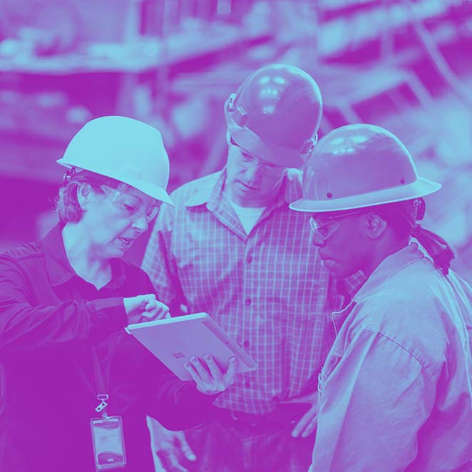 Workers in hardhats look at a tablet computer. 