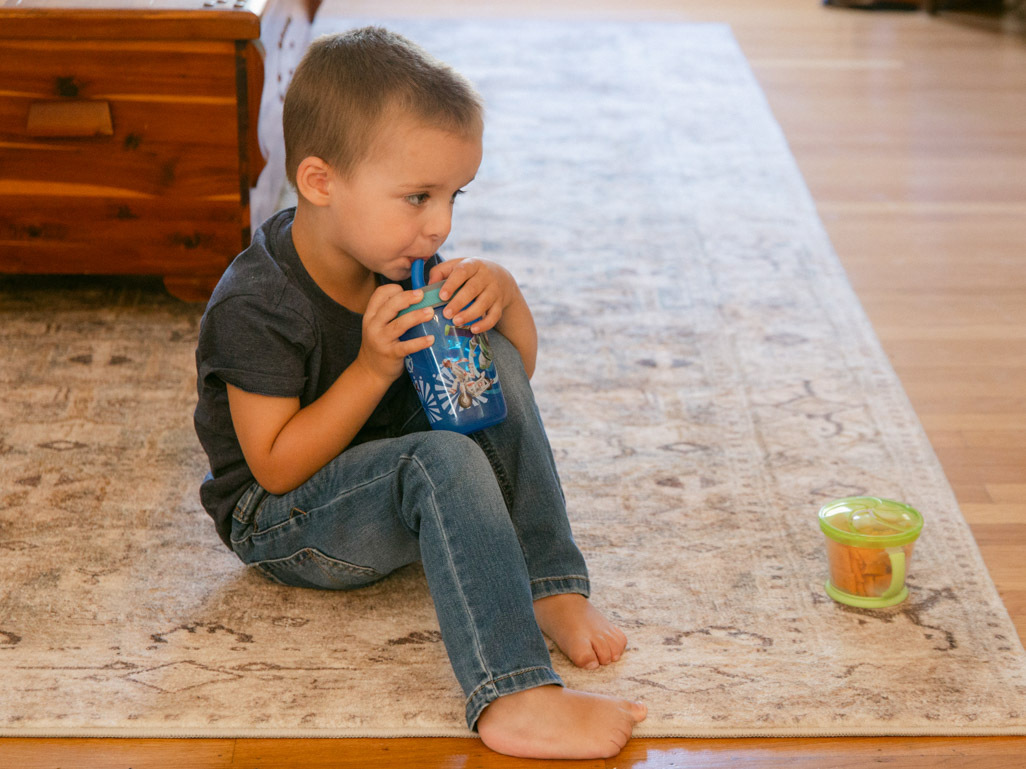 little boy sitting on carpet drinking water