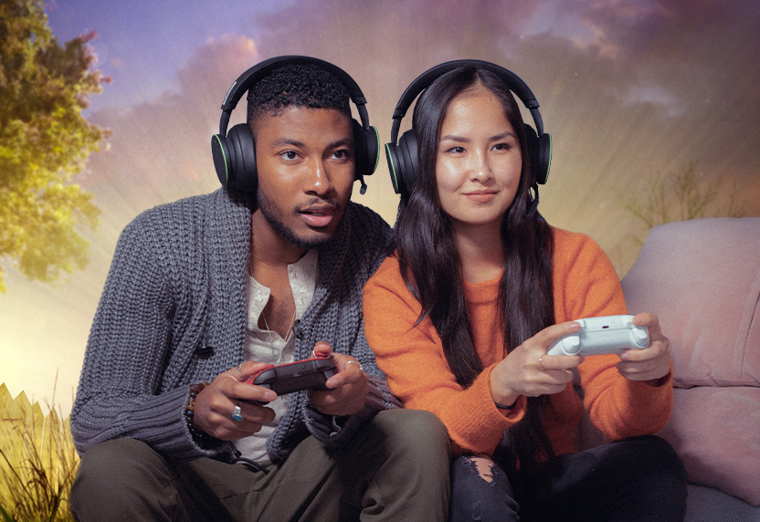 Twee personen met headsets zitten samen op een bank en spelen met Xbox-games