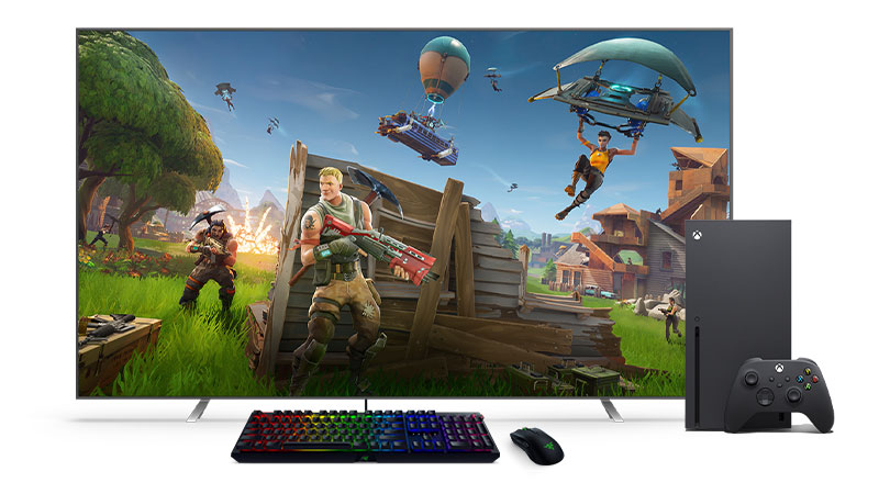 Egy fekete billentyűzet és egér egy Xbox Series X és egy TV előtt.