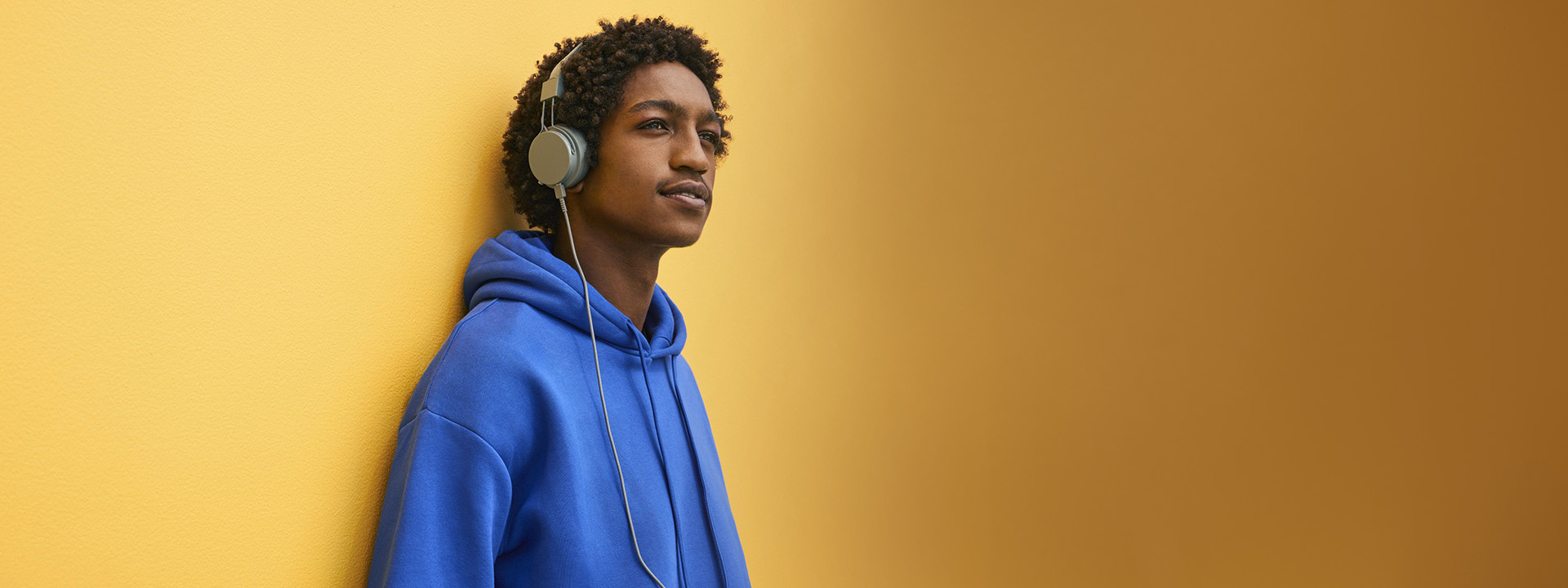 Teenager listening to music with headphones while leaning on a wall