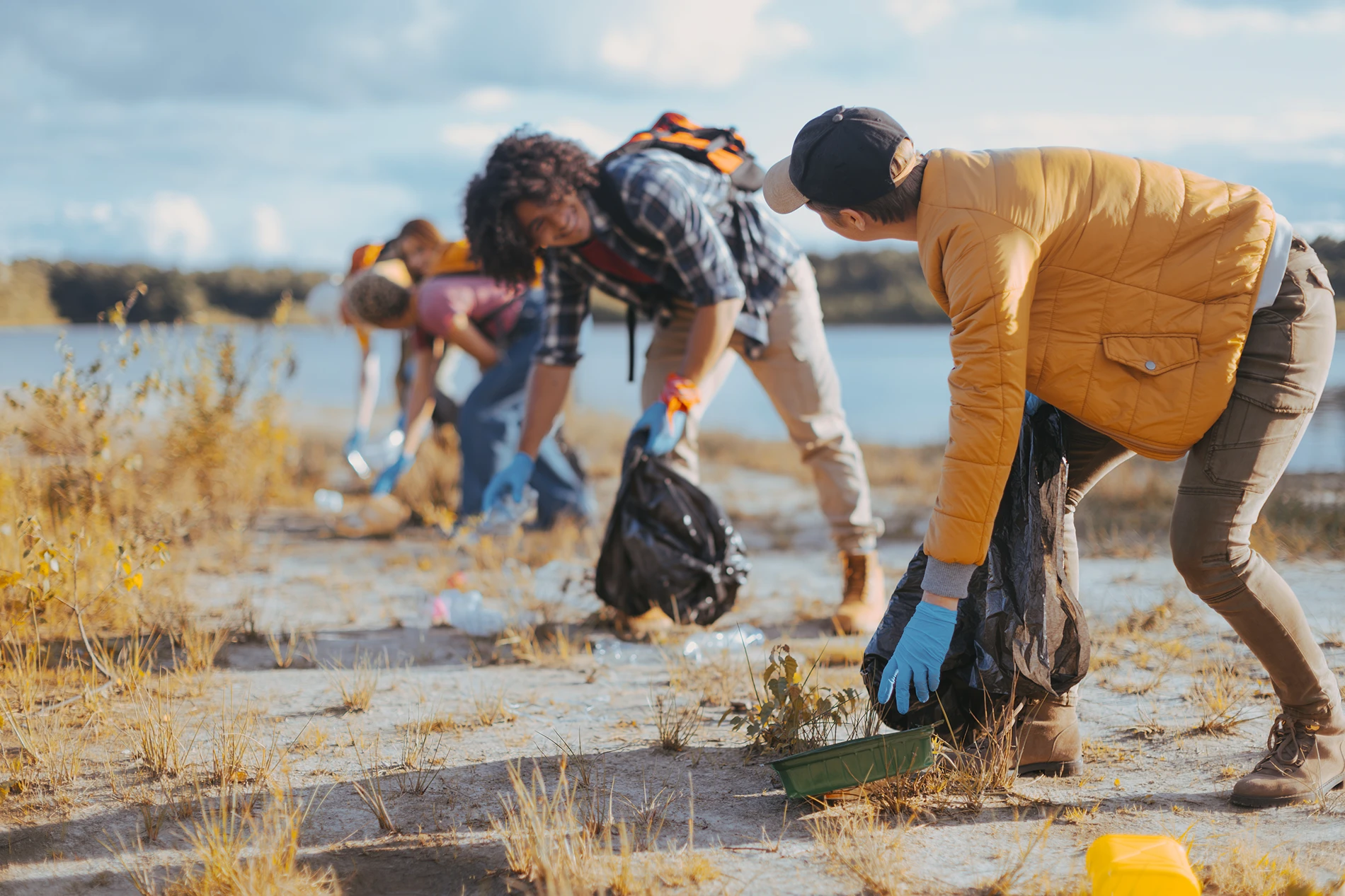 Volunteers participating in a waterside cleanup, picking up trash and supporting community involvement in cleaning up the environment.