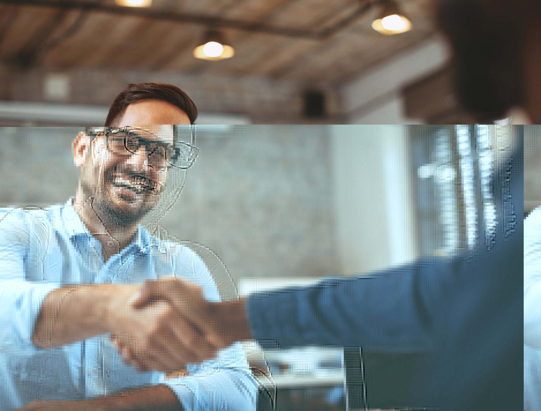 Smiling man reaching across a table to handshake another person in an office setting