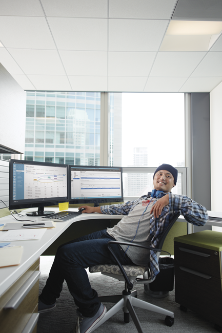 Person sitting at desk with two monitors talking with someone in the room