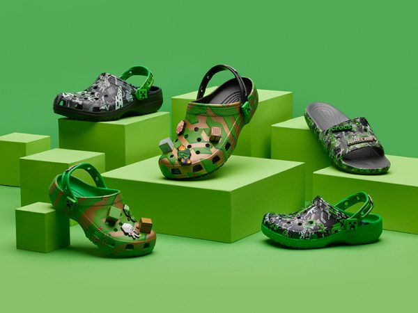 Five different styles if Crocs, several on blocks against a green background