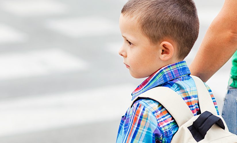 A boy and his mother wait to cross the street on their way to school.