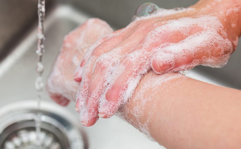 Unseen woman washing her hands with soap in a sink.