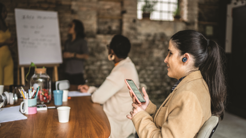 Businesswoman with a vision disability using smartphone and earphones during business meeting