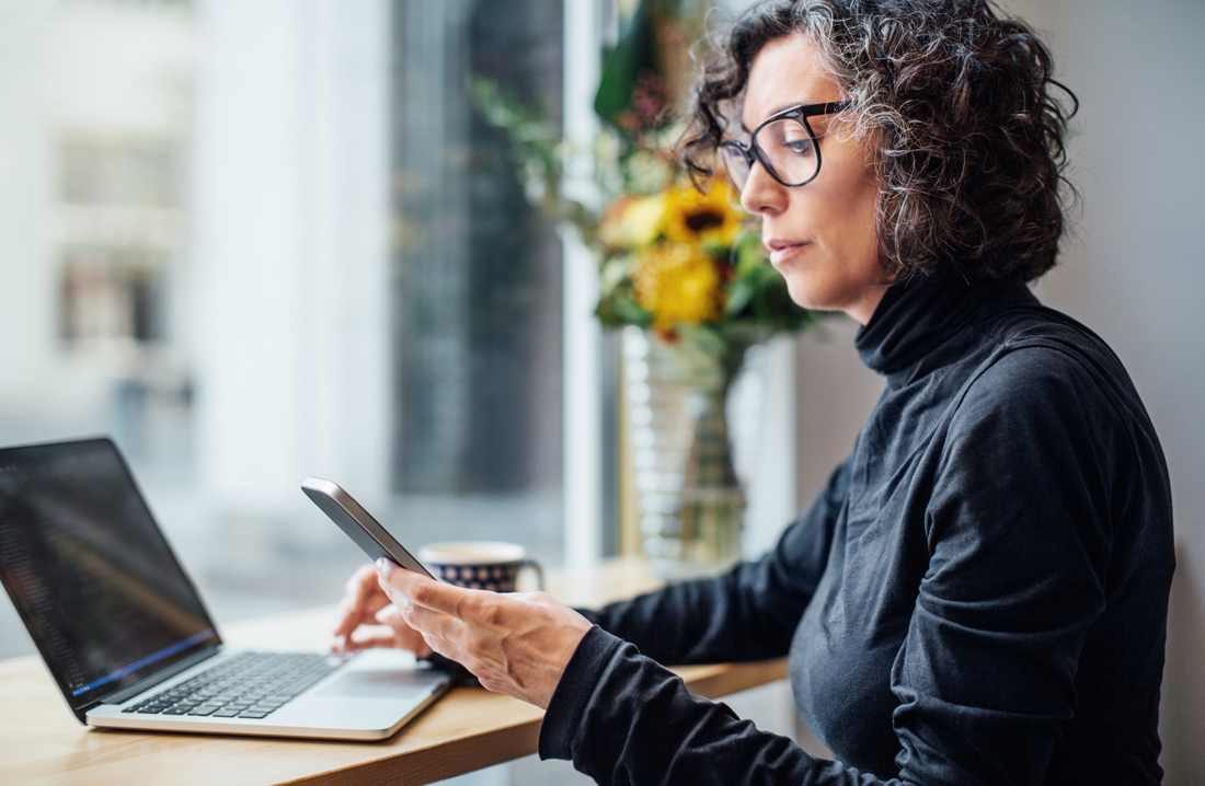 a woman works on her phone and laptop