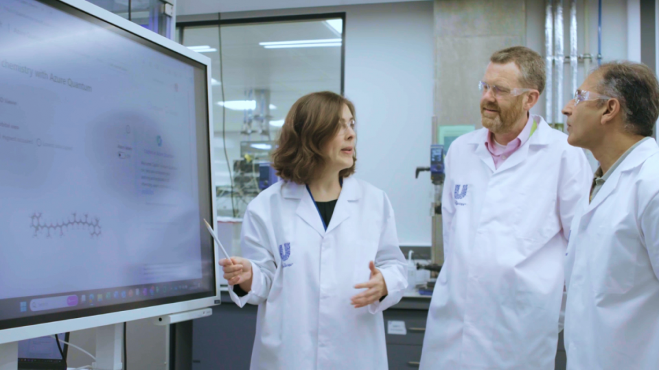 One woman and two men in while lab coats looking at a computer screen featuring Microsoft Azure Quantum Elements.