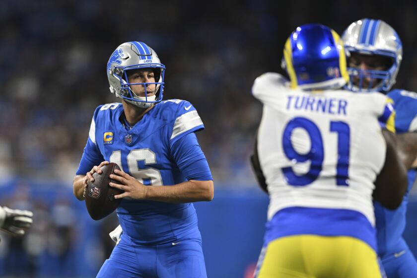 The Lions' Jared Goff (16) looks to pass as the Rams' Kobie Turner (91) rushes.