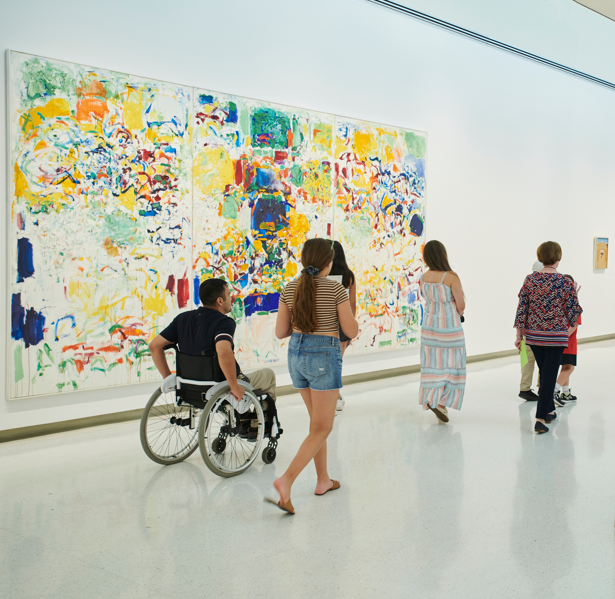 five people walking past a painting.