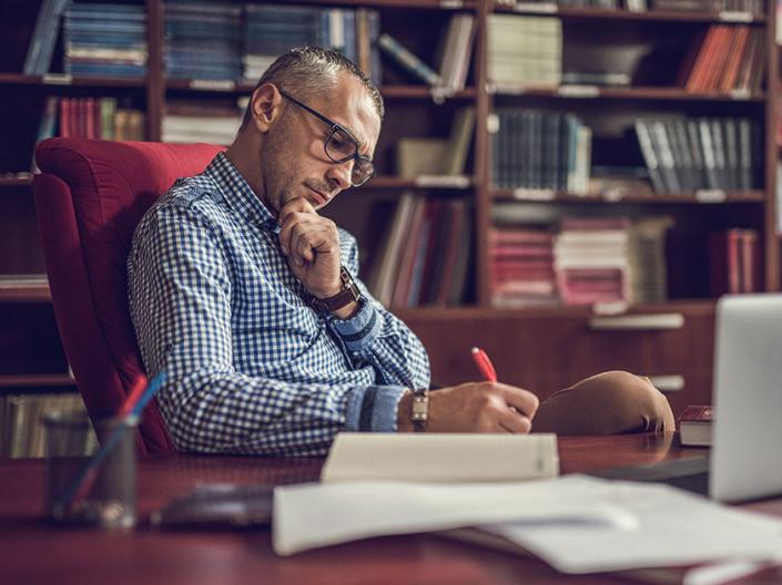 Man working from his home office with a stack of papers and his laptop