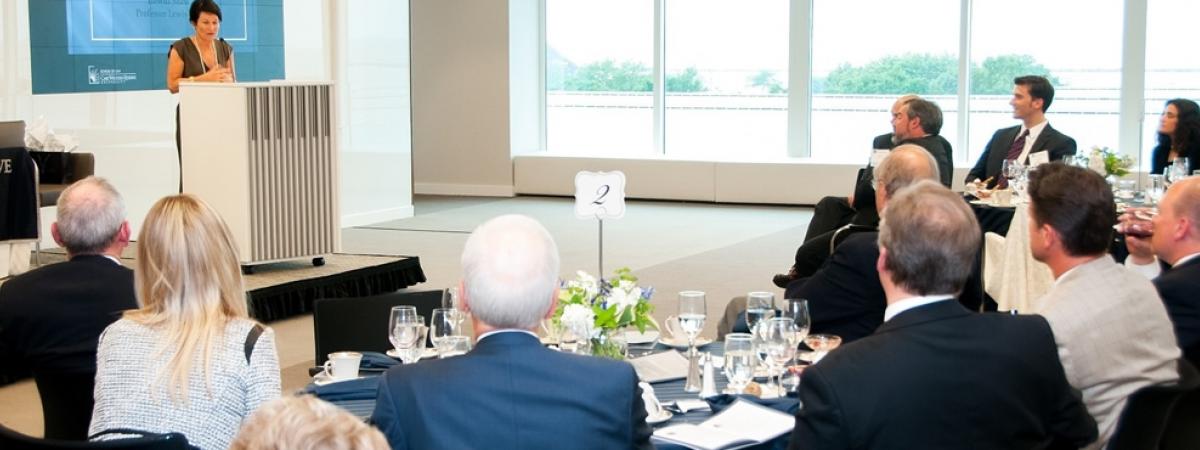 speaker giving a presentation to a group of professionals seated at formal dining tables